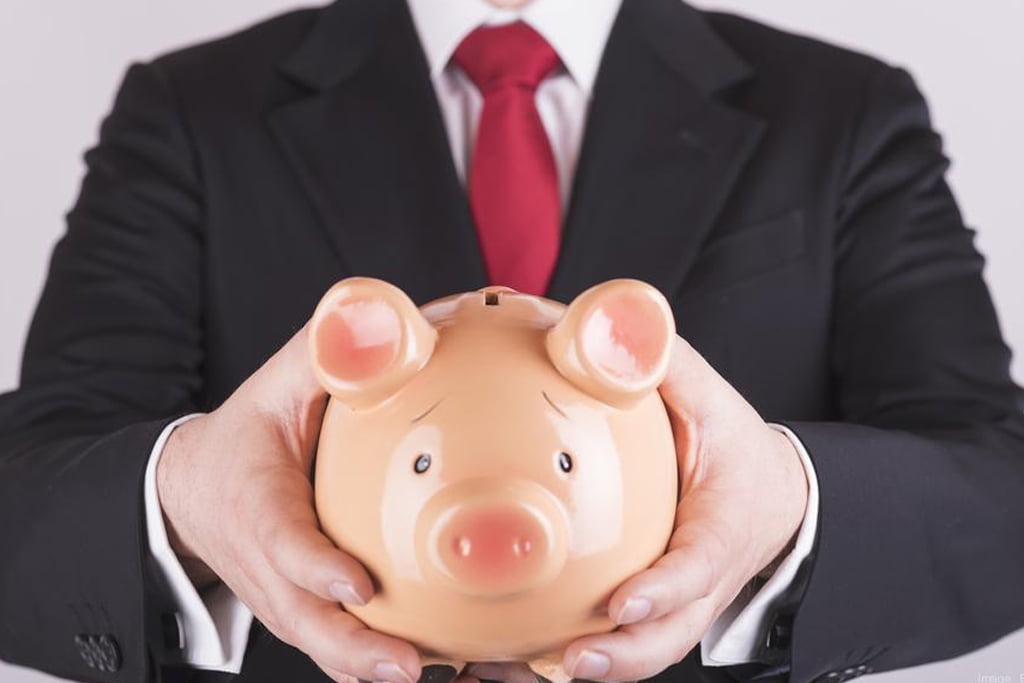 A man in black suit and red tie holding a piggy bank.