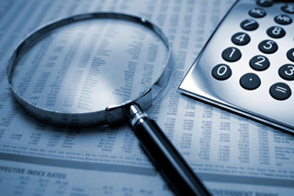 A magnifying glass and calculator on a financial document, symbolizing careful examination and calculations.