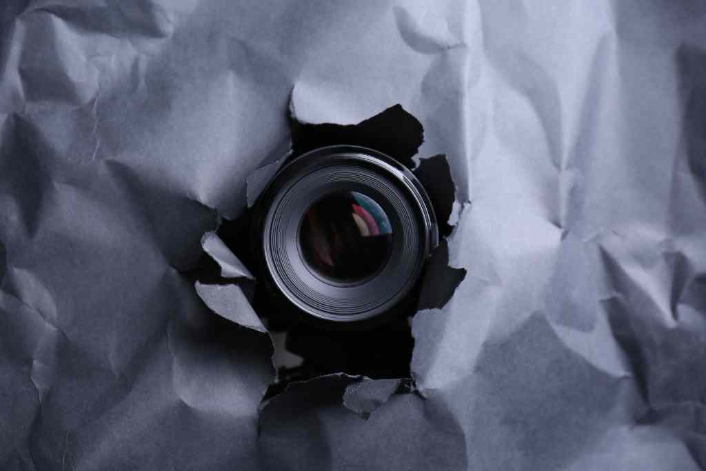 A camera peeks through a hole in a paper, capturing a unique perspective.