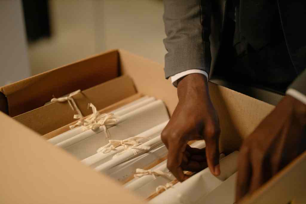 A man in a grey suit opening a box filled with papers, possibly important documents or files.