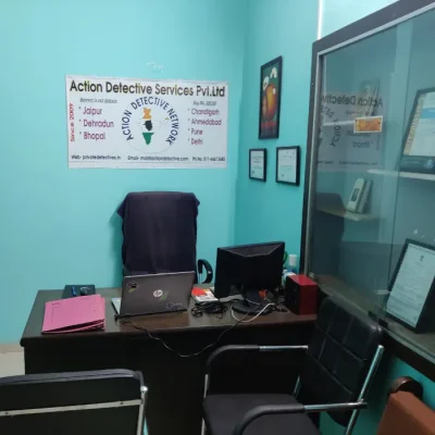 Office of Private Detective Agency In Jaipur - Action Detective. A brown table. three black chairs, a showcase with certification, monitor, laptop, a pink file and a banner visible