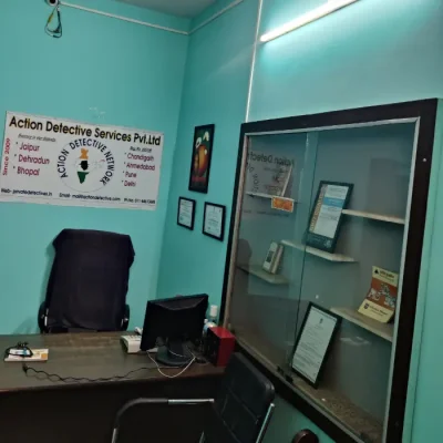 Office of Action Detective in Jaipur. A brown table. three black chairs, a showcase with certification, monitor, laptop and a banner visible