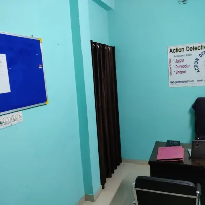 Office of Action Detective in Jaipur. A brown table. two black chairs, a pink file and a banner visible